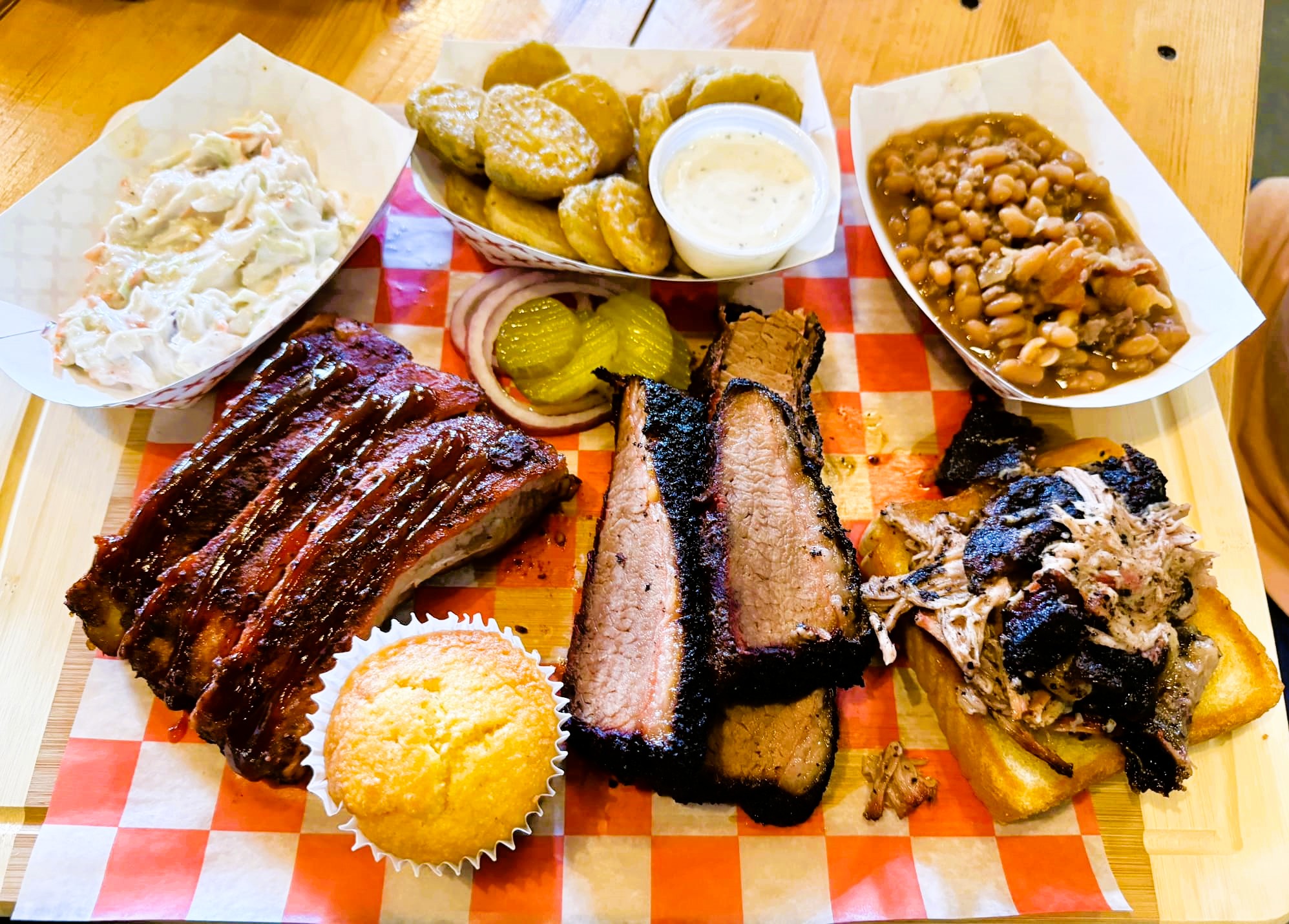 Platter of smoked brisket, ribs, cornbread and sides on a red checkered liner